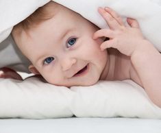 a baby laying under a white blanket on top of a bed with it's hands in the air