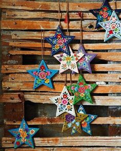 several colorful stars hanging from strings on wooden planks with flowers and leaves painted on them