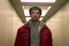 a man in a red jacket is looking at the camera while standing in a hallway