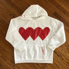 a white hoodie with red hearts on the front and back, sitting on a wooden floor