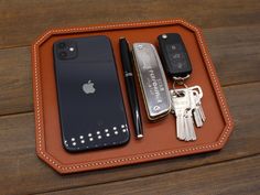 an apple phone and keys in a leather tray on a wooden table with keychains