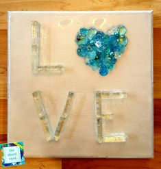 the word love is made out of glass blocks and beads on a white canvas with a blue heart