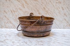 an old metal bowl with handles on a marble table