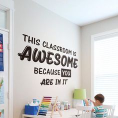 a young boy sitting at a desk in front of a wall decal that says this classroom is awesome because you are in it