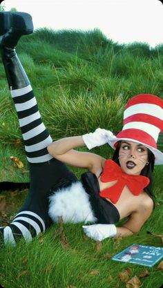 a woman dressed as the cat in the hat is laying on the grass with her legs spread out