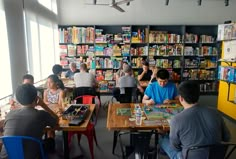 people are sitting at tables playing games in a library with bookshelves behind them