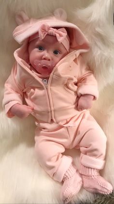 a baby is wearing a pink outfit and sitting on a fluffy white blanket with her hands in her pockets