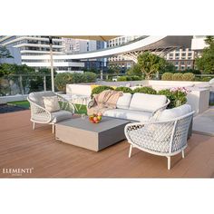 an outdoor living area with white wicker furniture and wooden flooring, surrounded by tall buildings