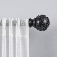 the curtain is closed and has a black ball on it's rod, along with white sheer curtains