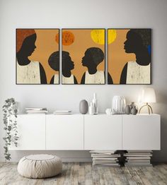 three paintings on the wall above a white sideboard in a room with wooden flooring