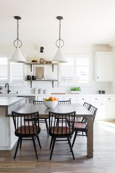 a kitchen table with four chairs and a bowl of fruit on the center island in front of it