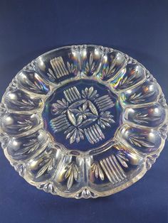 an ornate glass dish with spoons and forks in the center on a blue background