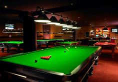 a green pool table in a dark room with several lights on the ceiling and bill tables