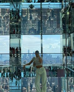 a woman standing in front of a glass wall looking at the city from inside a building