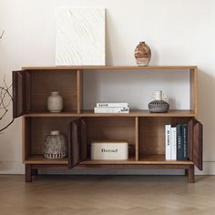 a wooden shelf with books and vases on it in front of a white wall