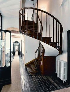 a spiral staircase in the middle of a room with wooden floors and white walls, along with black doors