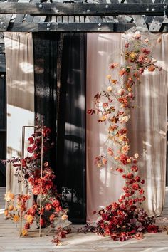 an arrangement of flowers and vines on display in front of a black backdrop with sheer drapes