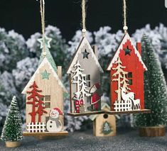 three wooden houses hanging from strings with christmas trees and snow on the ground in front of them