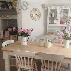 a kitchen table with chairs and flowers in vases on top of it, next to a wall clock