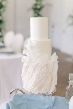 a white wedding cake sitting on top of a blue table cloth covered tablecloths