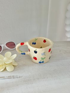 a white cup with cherries on it next to sunglasses and a flower shaped object