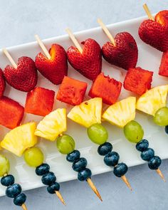 fruit skewers are lined up on a white platter with grapes, strawberries, and pineapples