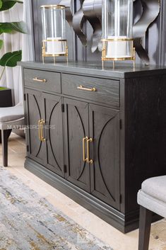 a black and gold sideboard with two lamps on top, next to a gray chair