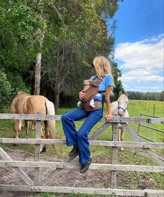 a woman is sitting on a fence with two horses