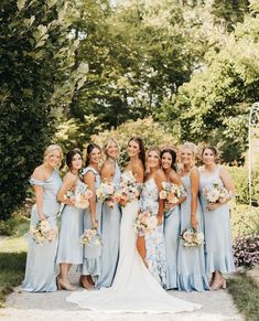 a group of women standing next to each other in front of trees and bushes with bouquets