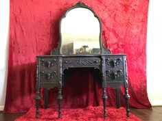 an antique vanity with a mirror on top of it in front of a red curtain