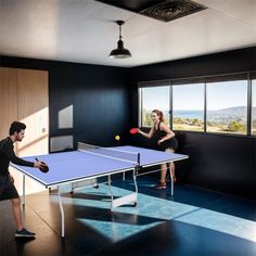 two people are playing ping pong in an empty room with blue walls and windows