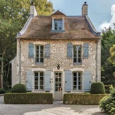 an old stone house with blue shutters on the front and side windows, surrounded by hedges