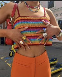 a woman in orange pants and a colorful crop top with rings on her hands, standing outside