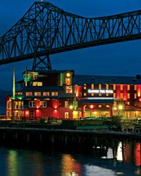 a large bridge spanning over a river next to a tall building with lights on it