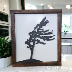 the silhouette of a pine tree is mounted in a wooden frame on a kitchen counter