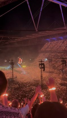 a large crowd at a concert with their hands up in the air and lights on