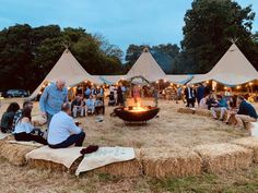 a group of people sitting around a fire pit in the middle of a field with hay bales