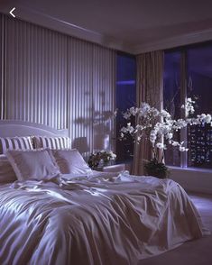 a bed with white sheets and pillows in a bedroom next to a window at night