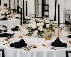 the table is set with white flowers and black napkins, gold place settings and candles