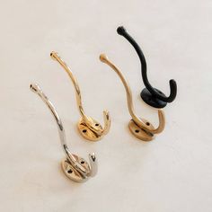 three different colored metal hooks on a white surface with one black hook and one gold hook