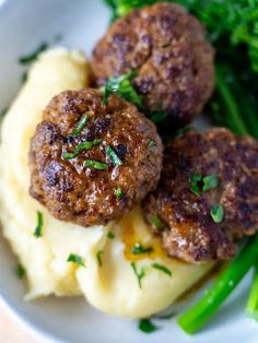 two meatballs and mashed potatoes on a plate with broccoli in the background