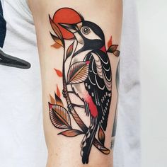 a colorful bird tattoo on the right arm and lower arm, with leaves around it