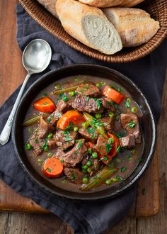 a bowl filled with beef and carrots next to bread