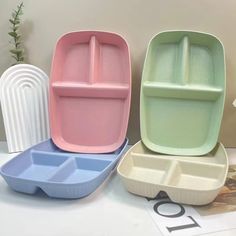 three different colored trays sitting next to each other on a white counter top with flowers in the background