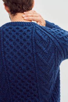 a man with his back turned to the camera wearing a blue sweater and holding his hand on his shoulder