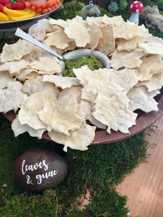 chips and guacamole on a platter with a bowl of fruit in the background