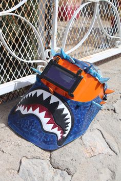 an orange and blue bag with a shark's mouth on it sitting in front of a fence