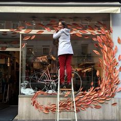 a woman is standing on a ladder in front of a store window and talking on her cell phone