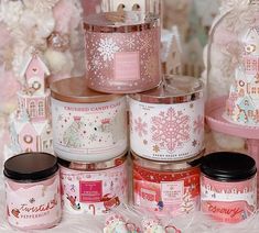 many different types of candles are displayed on a white furnishing with pink snowflakes