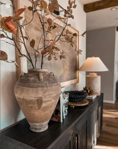 a vase sitting on top of a wooden table next to a lamp and pictures hanging on the wall